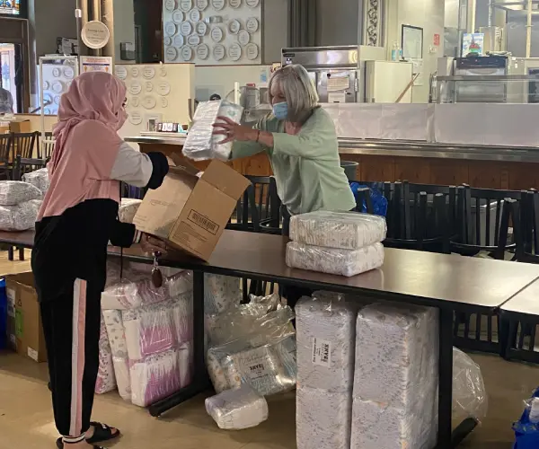 A woman in a hijab is handing boxes to another person.