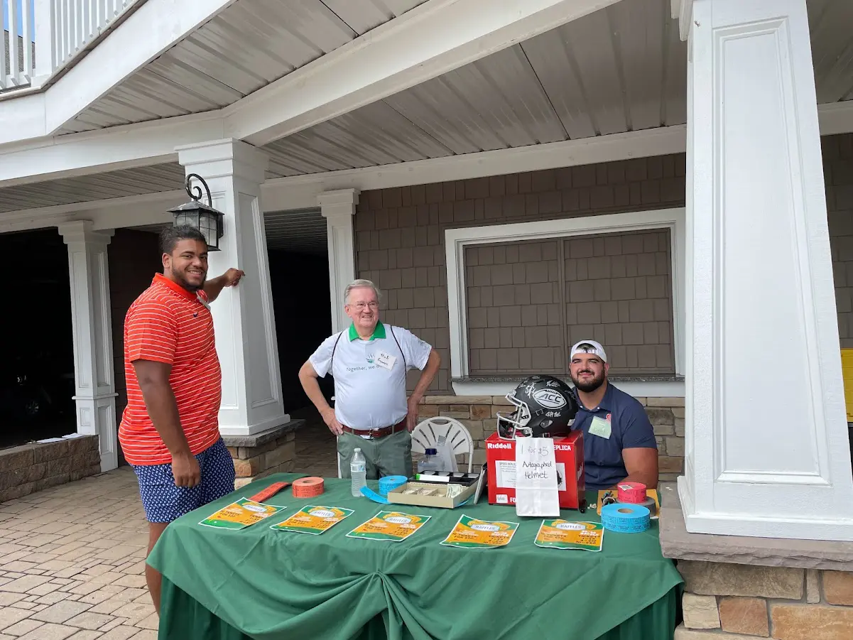 SU Football players stand with volunteer Bob Graves selling raffle tickets.