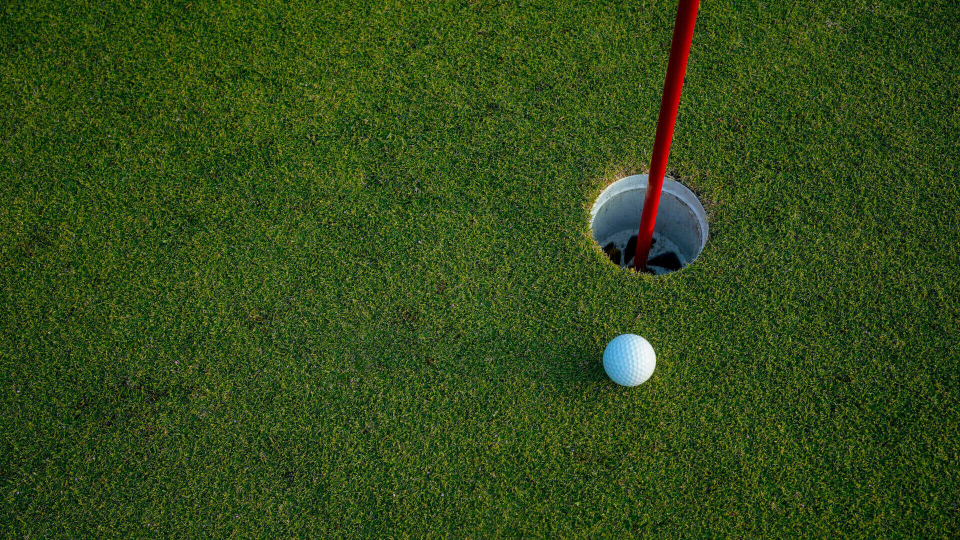 Golf ball near hole on green grass.