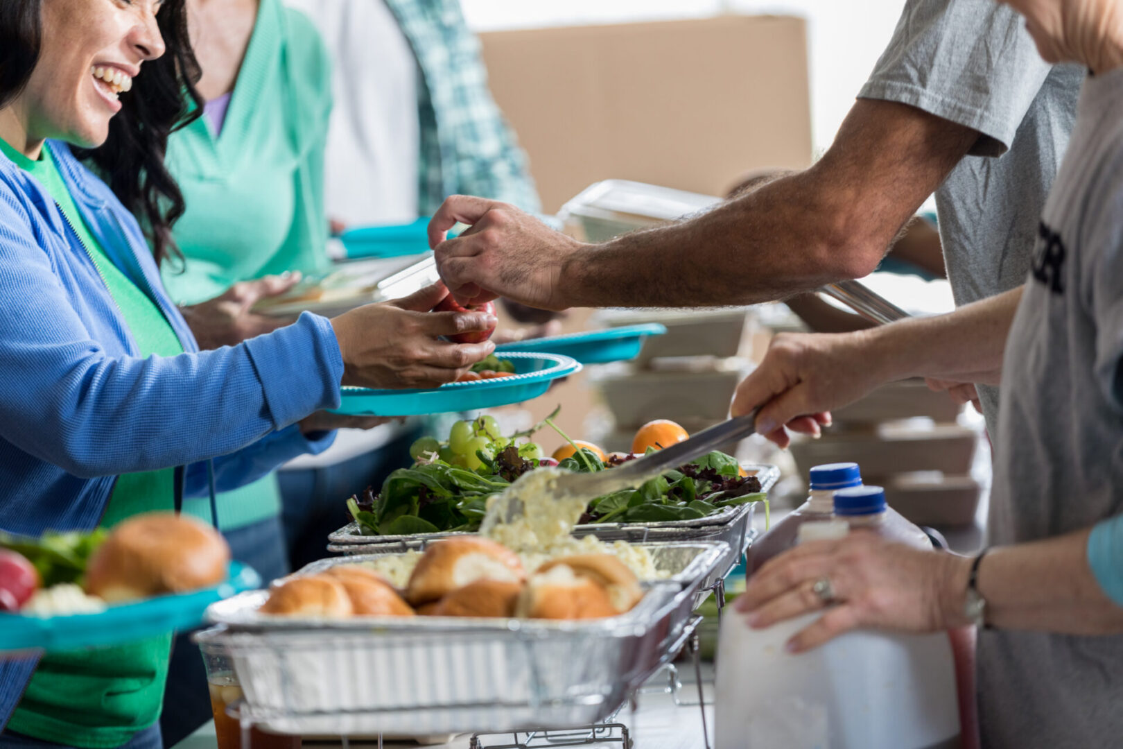 Happy Hispanic woman receives meal at soup kitchen. Volunteers are serving people in line.
